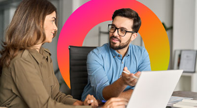 Two people having a discussion in an office setting, sitting behind a laptop