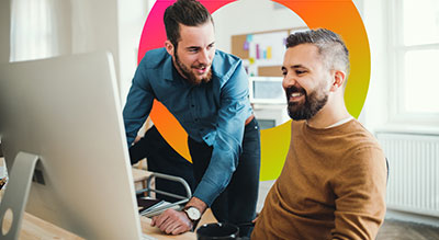 Two individuals collaborate behind a computer monitor in a modern office